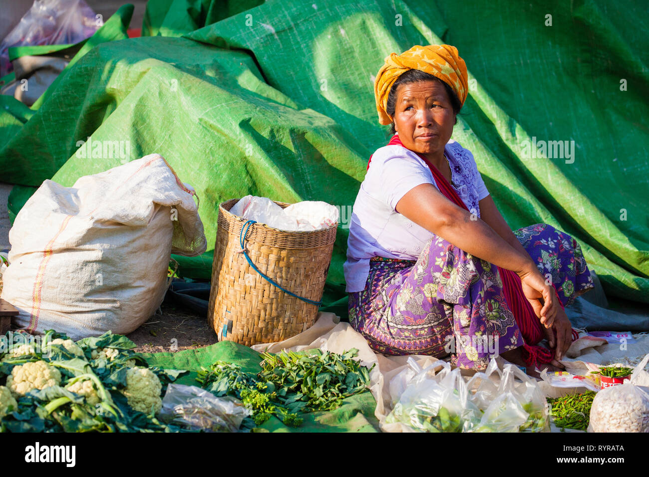 Una donna si siede su un telone verde vendere verdure a Kalaw mercato, Myanmar Foto Stock