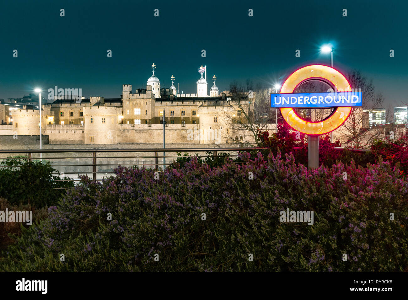 Tower Hill, Londra, Inghilterra, 14 marzo 2019. Un famoso London Underground insegna illuminata lato uscita stazione di Tower Hill con la Torre di Londra in b Foto Stock