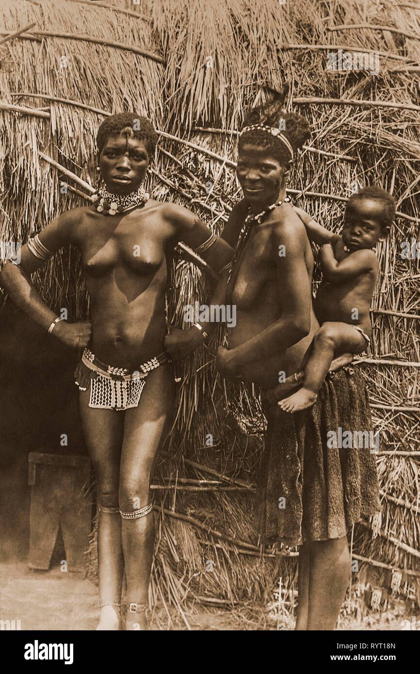 Due donne africane con un bambino piccolo sul loro retro davanti alla loro capanna, 1912, Durban, Sud Africa Foto Stock