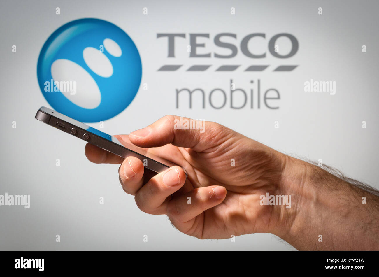 Un uomo con un telefono cellulare nella parte anteriore del Tesco Mobile network sign Foto Stock