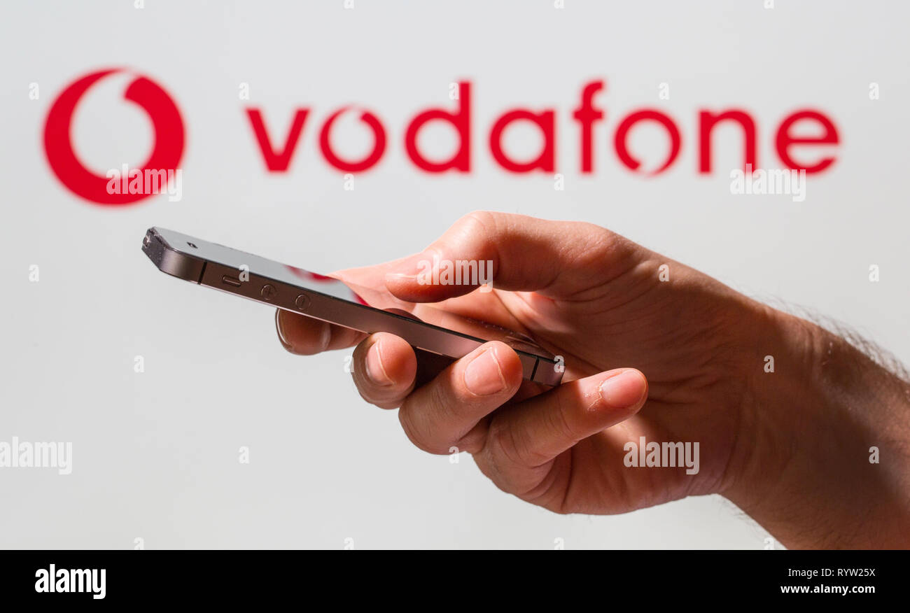 Un uomo con un telefono cellulare di fronte a Vodafone logo di segno Foto Stock
