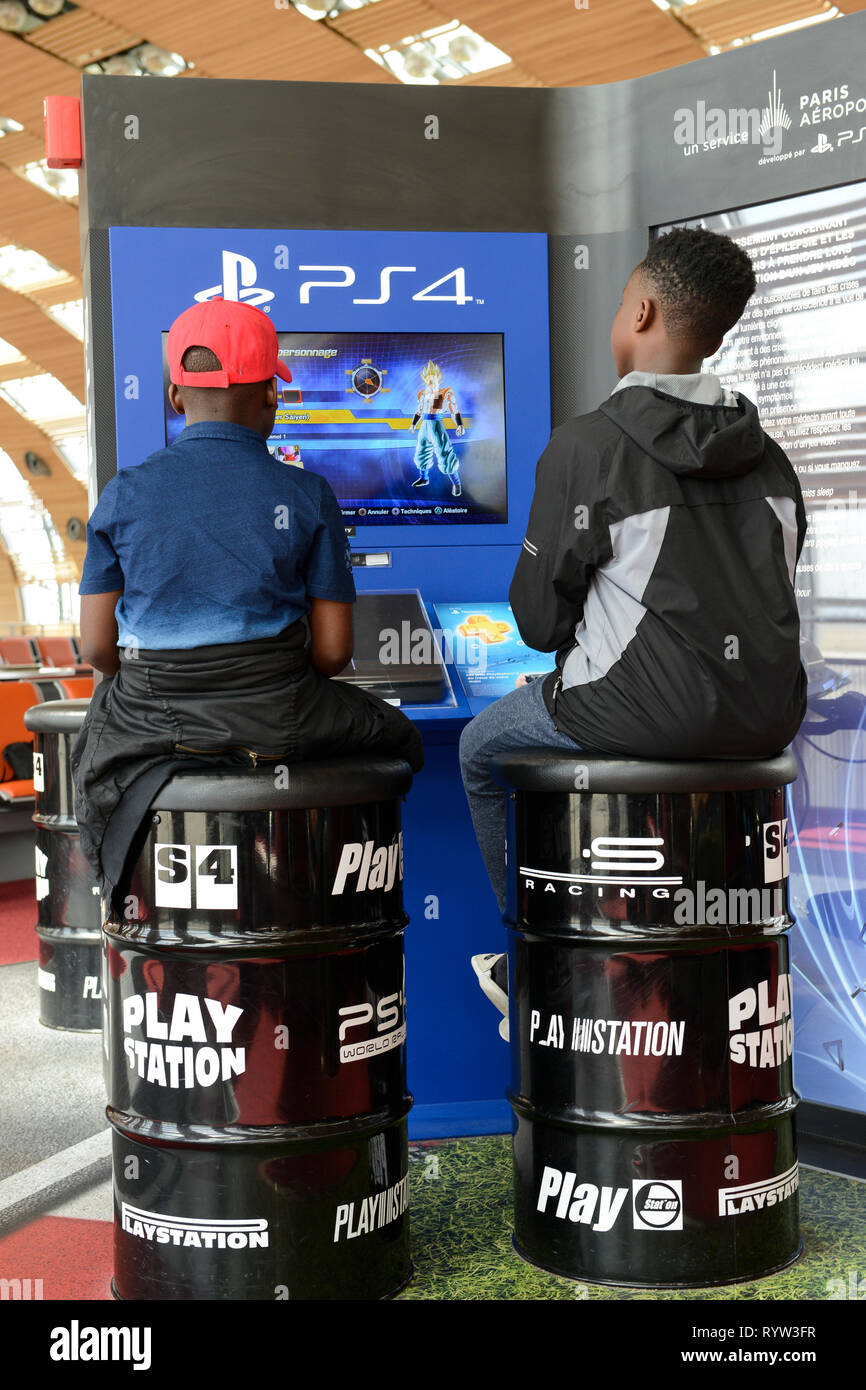 Francia, Parigi Charles de Gaulle, due ragazzi africani seduto sulla canna di stagno e gioco Sony PS4 Playstation in area di attesa alle porte Foto Stock