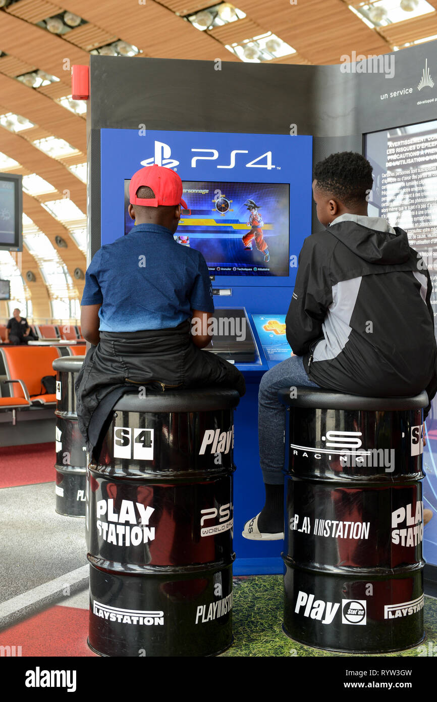 Francia, Parigi Charles de Gaulle, due ragazzi africani seduto sulla canna di stagno e gioco Sony PS4 Playstation in area di attesa alle porte Foto Stock