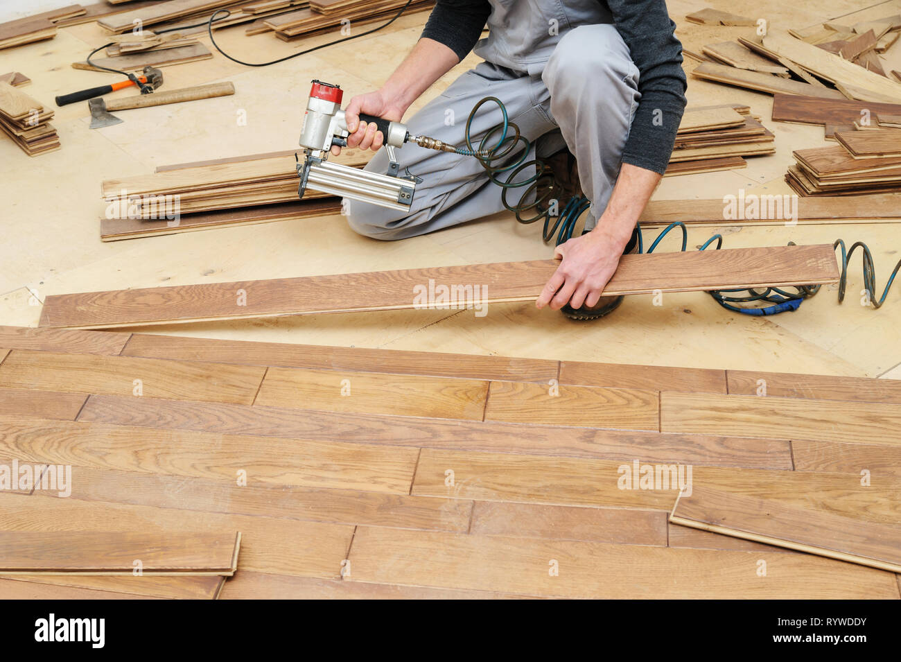 Installazione di un pavimento in legno. Un lavoratore fissa la scheda  utilizzando una pistola sparachiodi Foto stock - Alamy