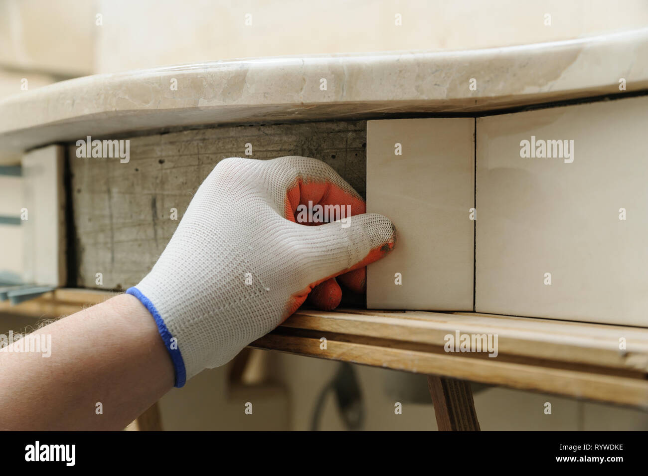 Del lavoratore mette mano il pezzo di tegola sulla parete curva sotto un lavandino. Foto Stock