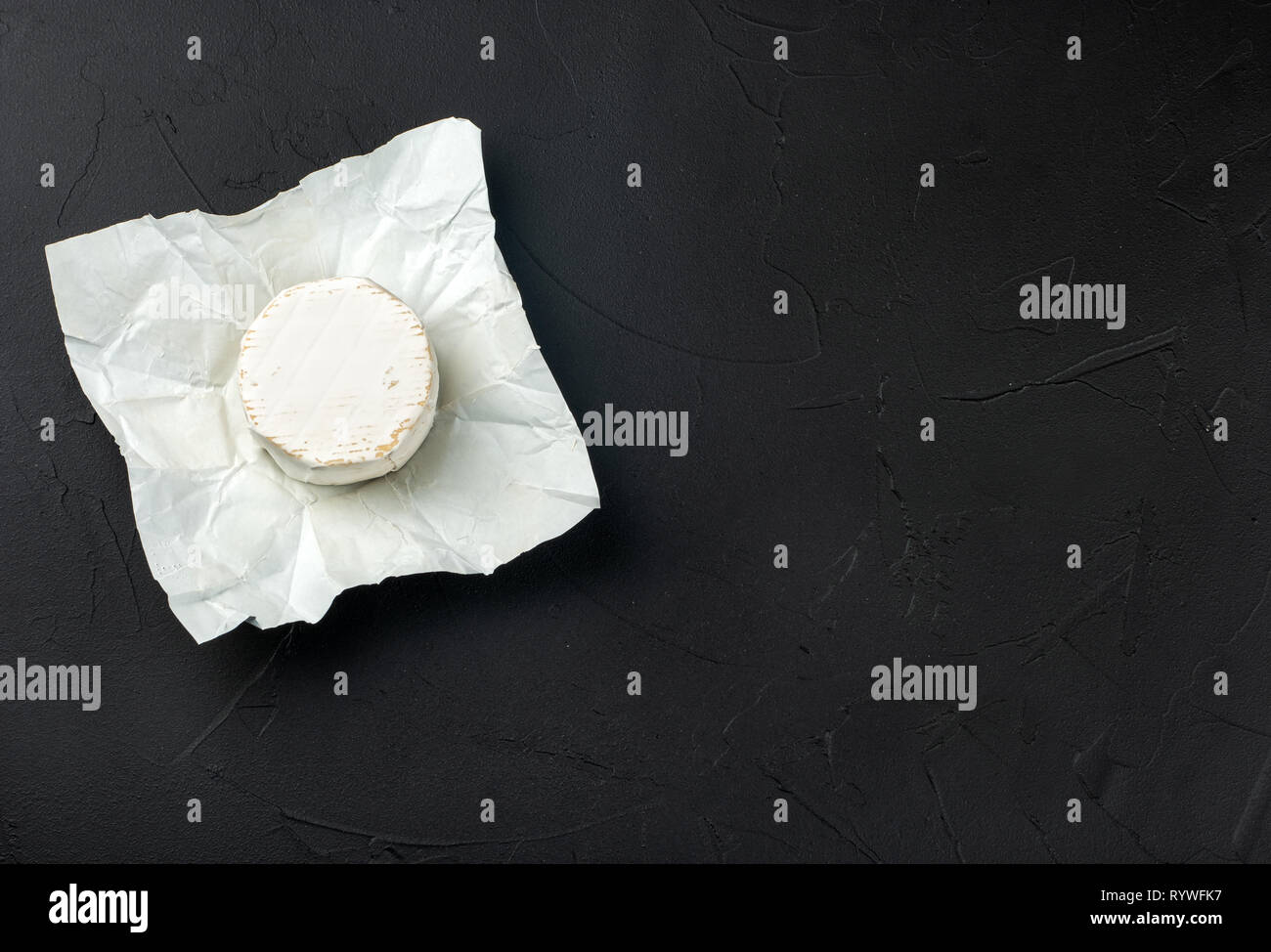 Round Formaggio Brie in aprire il pacchetto di carta sul calcestruzzo scuro sfondo, vista dall'alto Foto Stock