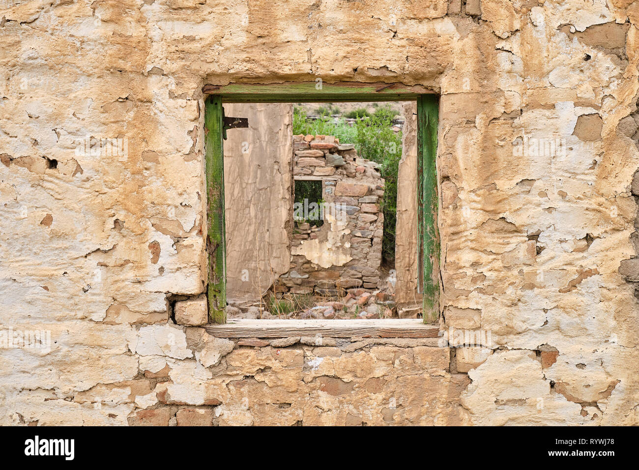 Vuoto centrale verde sul telaio di una finestra sulla parete rocciosa di casa abbandonata. Attraverso il telaio vedere pareti sbriciolato rimanente di casa in rovina Foto Stock