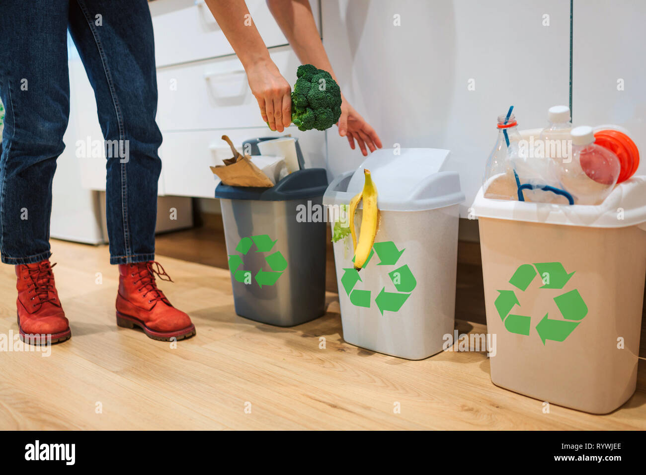 La separazione dei rifiuti a casa. Vista ritagliata della donna mettendo i broccoli nella spazzatura. Cestino colorato bidoni per lo smistamento dei rifiuti in cucina Foto Stock