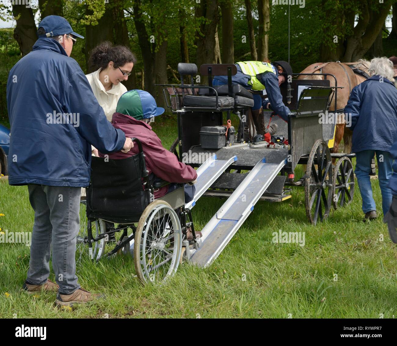In sedia a rotelle rider essendo spinto verso l'alto una rampa su un carrello su una carrozza a giorno eseguire dall'equitazione per disabili Associazione, Wiltshire, Regno Unito. Foto Stock