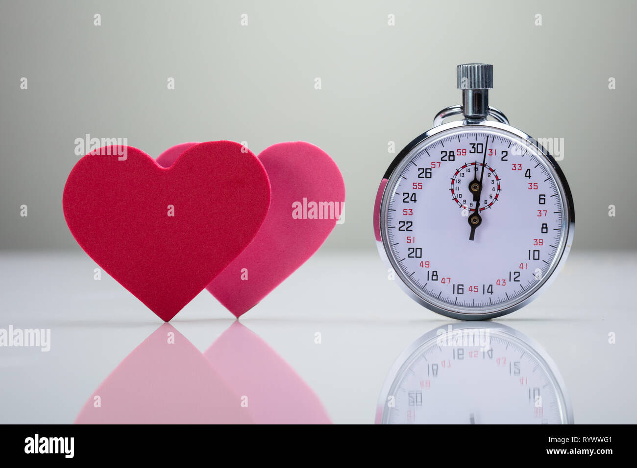 La riflessione del rosso e del rosa forma di cuore con il cronometro sulla scrivania bianca Foto Stock