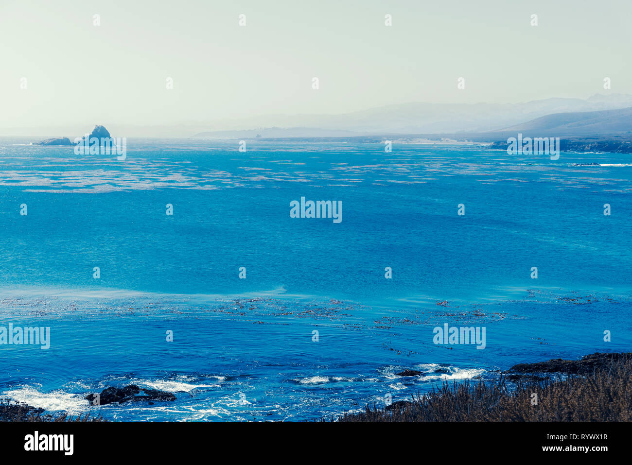 Affacciato sul blu del mare con onde che si infrangono sulla spiaggia rocciosa al di sotto. Foto Stock