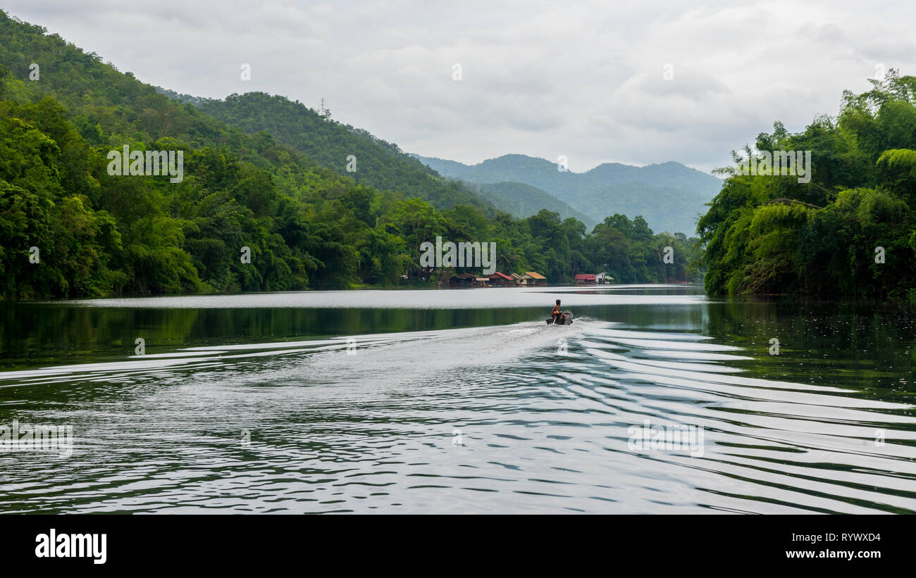 Uomo in tailandese tradizionale andando in barca lungo il fiume nella foresta Foto Stock