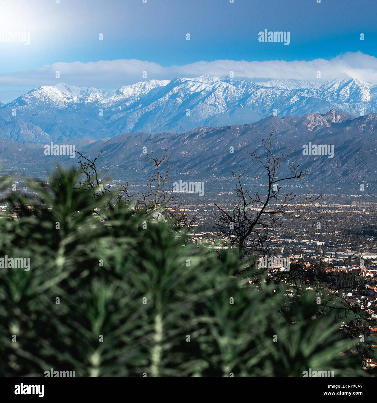 Una coperta di neve Mountain Range sullo sfondo di un paesaggio urbano suburbano in primo piano. Le nuvole provenienti dalla sommità della montagna innevata. Foto Stock