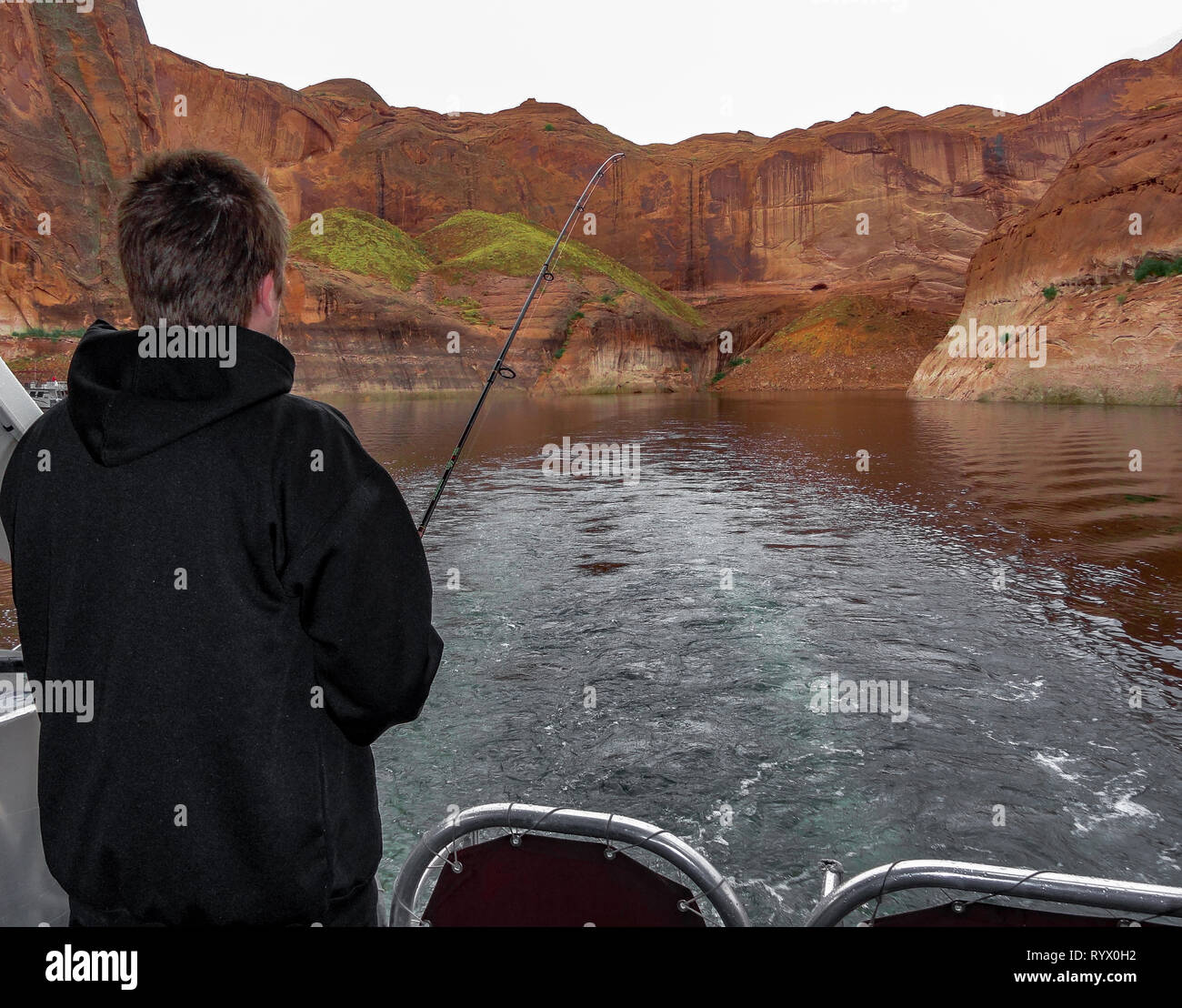Un uomo pesca al largo della parte posteriore di una barca sul lago nel deserto. Foto Stock