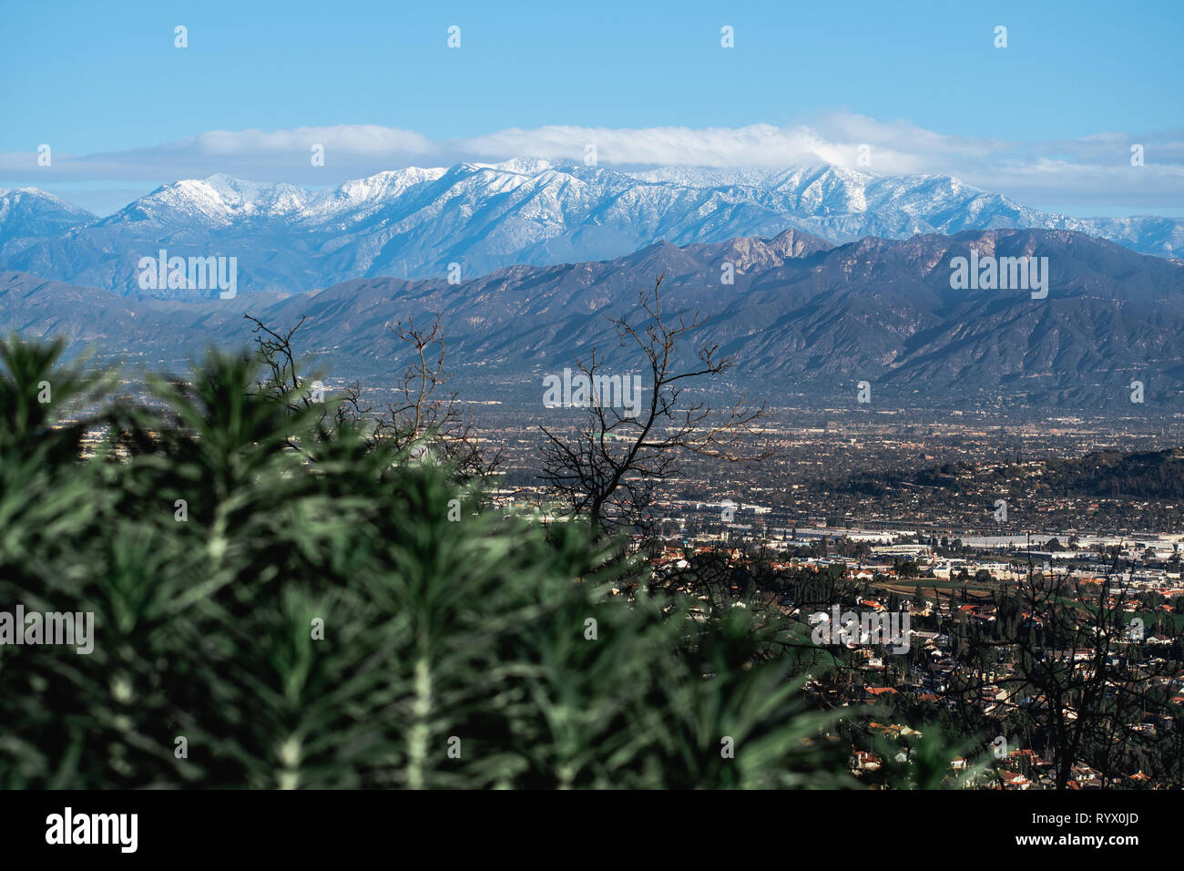 Una coperta di neve Mountain Range sullo sfondo di un paesaggio urbano suburbano in primo piano. Le nuvole provenienti dalla sommità della montagna innevata. Foto Stock