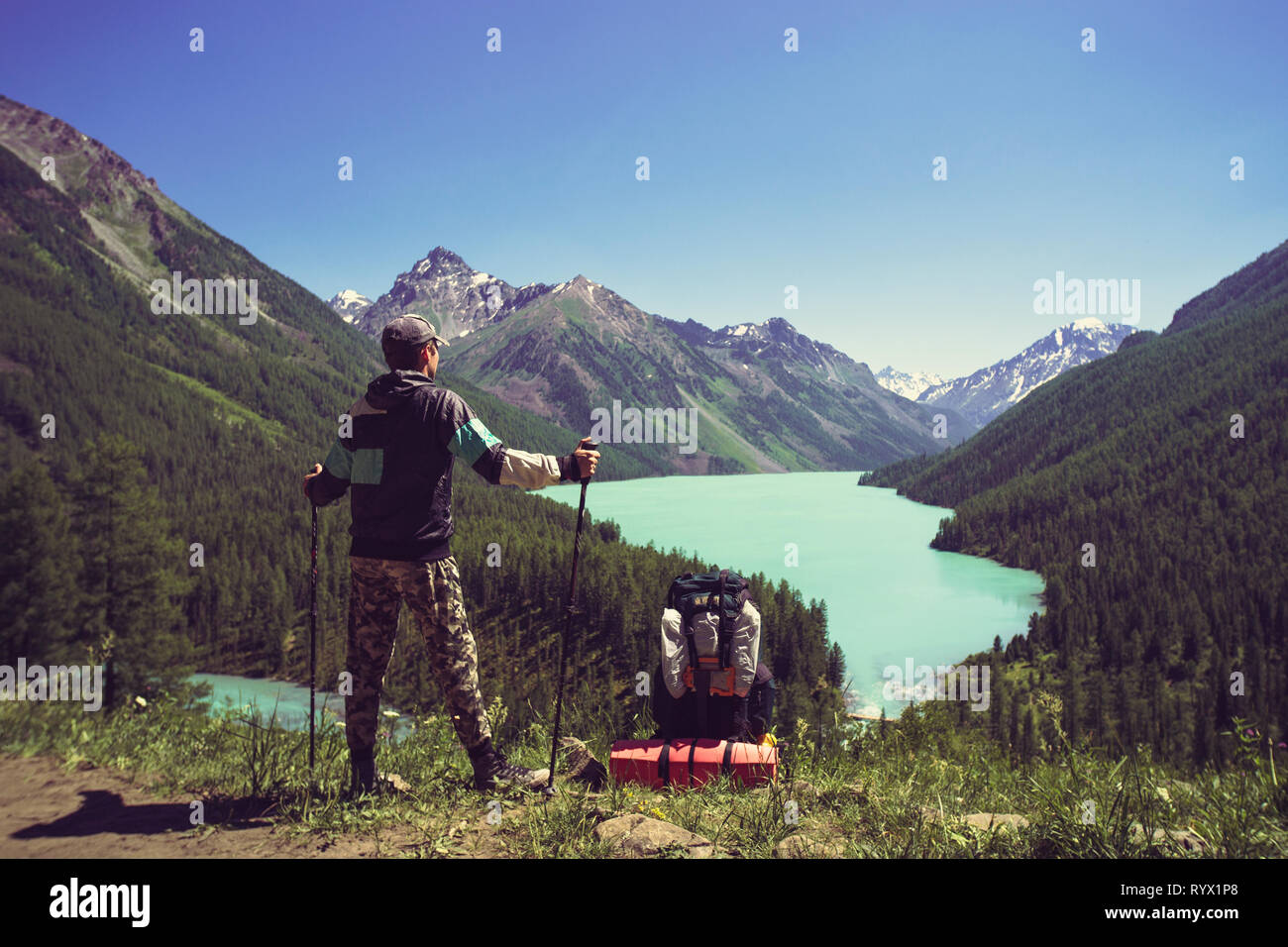 Foto dal retro del turista uomo con bastoni da passeggio con le mani in alto sulla collina vicino lago. azienda turistica di bastoni per Nordic walking Foto Stock