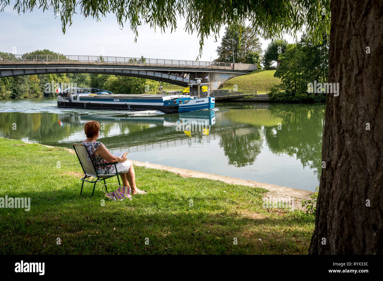 Barcone sul fiume Aisne in Choisy au Bac, nel dipartimento Oise (Francia settentrionale). In primo piano, una vecchia donna seduta su una sedia da campeggio, readin Foto Stock