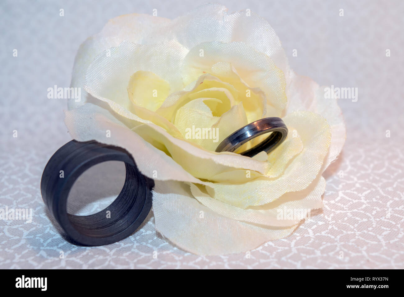 Gli anelli di nozze fatta da acciaio di Damasco visualizzato su una seta gialla fiore di nozze con sfondo bokeh di fondo. Foto Stock