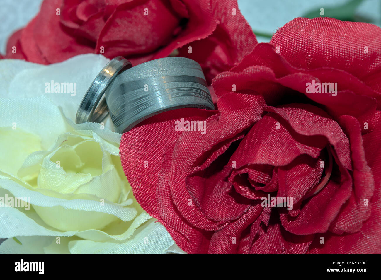 Acciaio damasco wedding bands accoccolato tra il rosso e il giallo di seta fiori matrimonio e un bokeh sfondo. Foto Stock