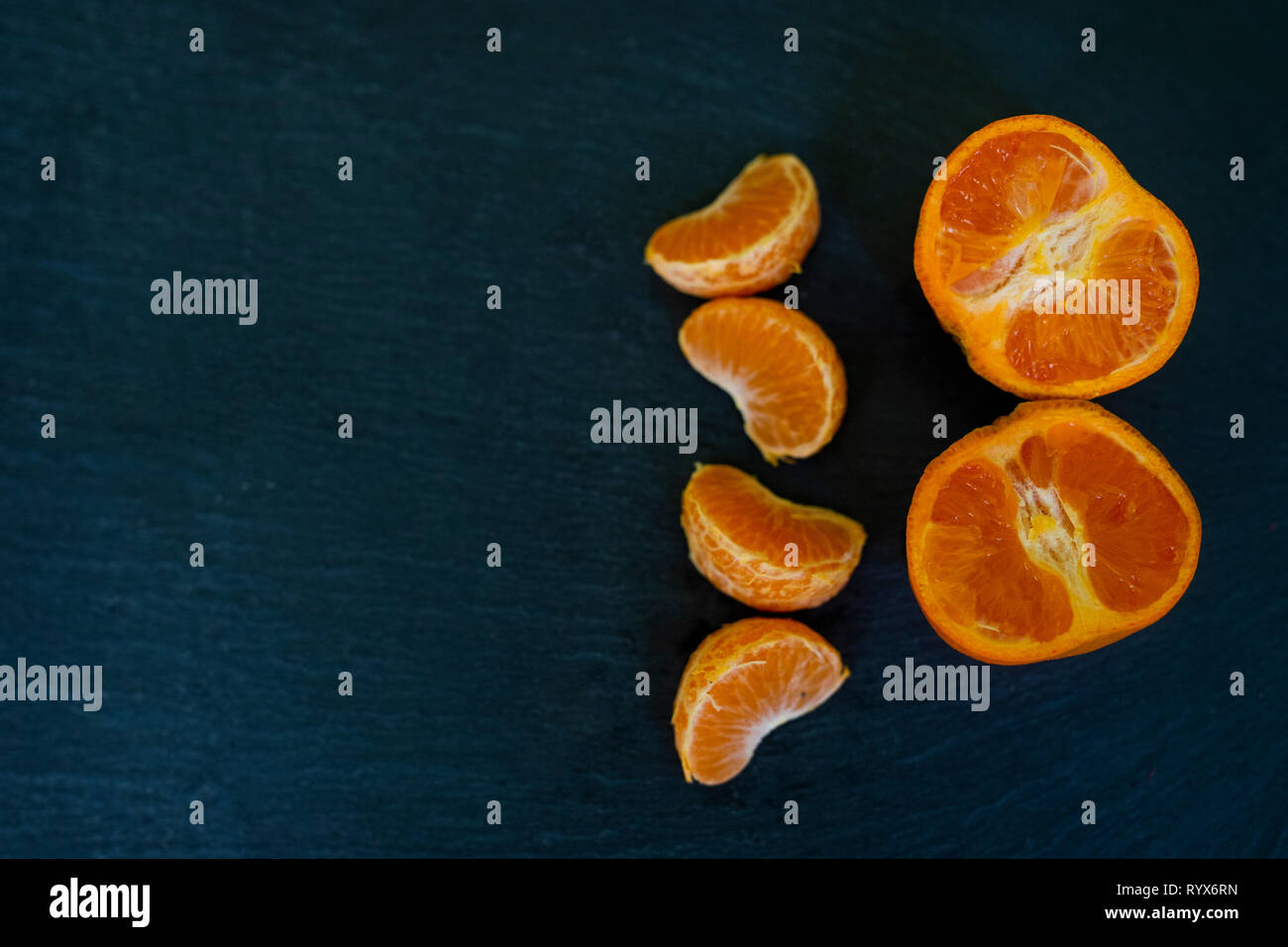 I mandarini satsuma/arancione/clementina vicino fino al buio su un sfondo di ardesia tagliati a metà Foto Stock