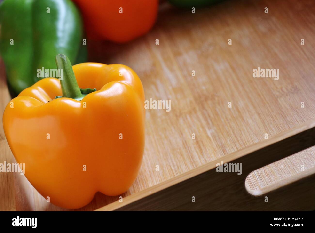 Freschi peperone giallo su cucina in legno vassoio. Arancione e peperoni verdi sfocate in background. Ingredienti Foto Stock