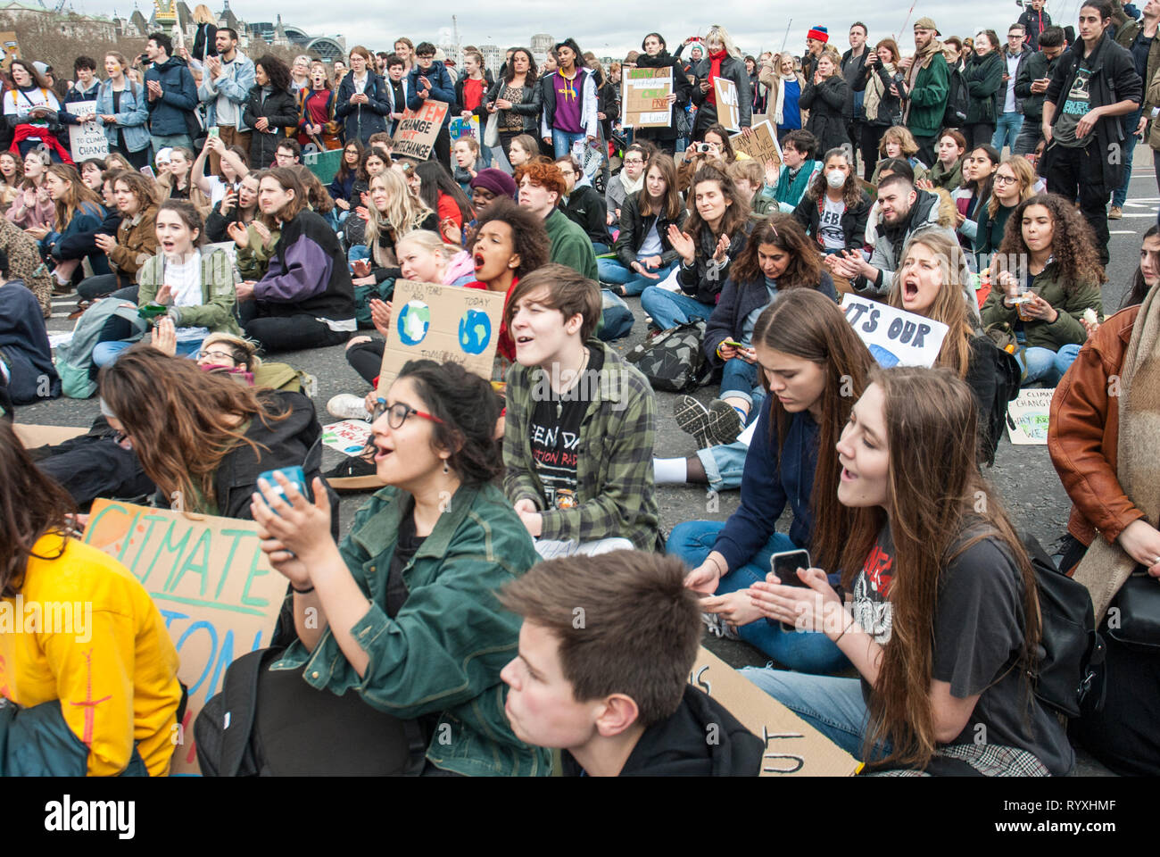 Londra, Regno Unito. Il 15 marzo, 2019. Gli studenti della scuola di campagna contro il cambiamento climatico il blocco Westminster Bridge Credito: Maggie sully/Alamy Live News. I bambini della scuola in sciopero, parte del 'FridaysforFuture' protestare contro il cambiamento climatico si raccolgono al di fuori del Parlamento, Londra e hanno un sedersi protesta sul Westminster Bridge bloccando a tutti attraverso il traffico. Vi è stato quindi un vivace incontro con molti giovani oratori affrontare le preoccupazioni dei giovani sulla giustizia climatica e il riscaldamento globale. Foto Stock