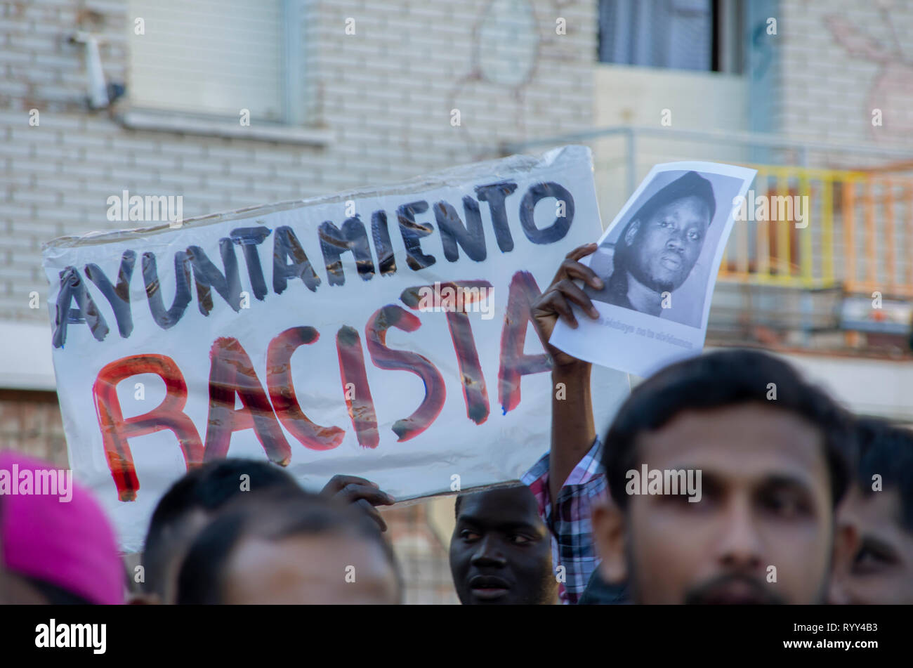 Una targhetta che dice "razzista governo locale" e il ritratto di Mame Mbaye visto durante la protesta. La protesta contro il razzismo istituzionale ha avuto luogo a Nelson Mandela Square a Madrid un anno dopo la morte di Mame Mbaye, un senegalese venditore ambulante che morì mentre viene inseguita dalla polizia per la vendita sulle strade. Secondo i manifestanti il giovane non hanno alcun documenti legali pur avendo speso più di dieci anni in Spagna e le autorità non ha aiutato la sua famiglia dopo la sua morte. Essi hanno anche reso omaggio alle vittime della Nuova Zelanda attacco terroristico nelle moschee. Foto Stock