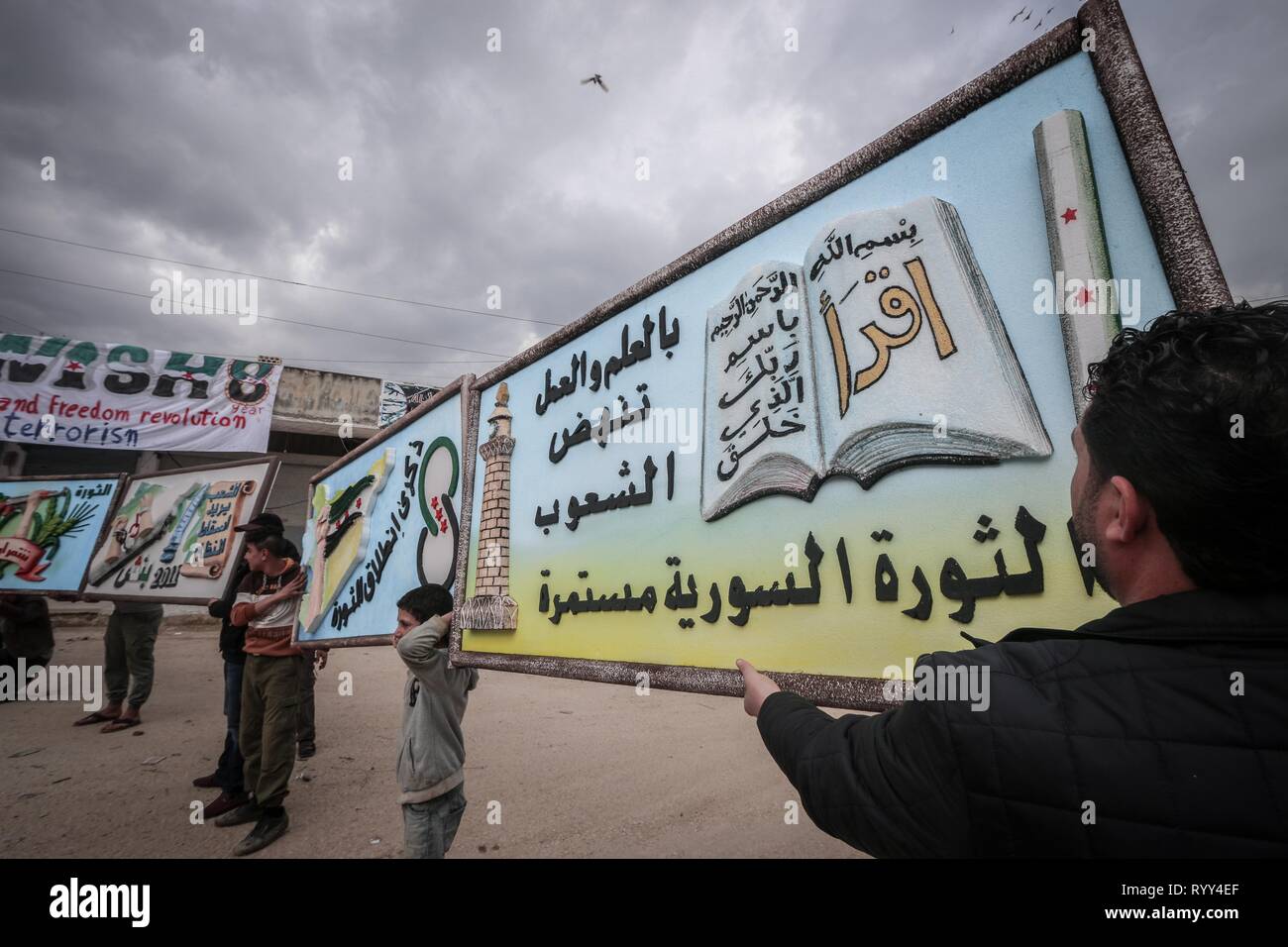 Siri sono visti i banner di contenimento durante la celebrazione. Siri nella città di Bensh, che si trova a est di Idlib e controllati dall'opposizione, celebrato l'ottavo anniversario della rivolta contro il regime del Presidente Bashar al-Assad. Foto Stock
