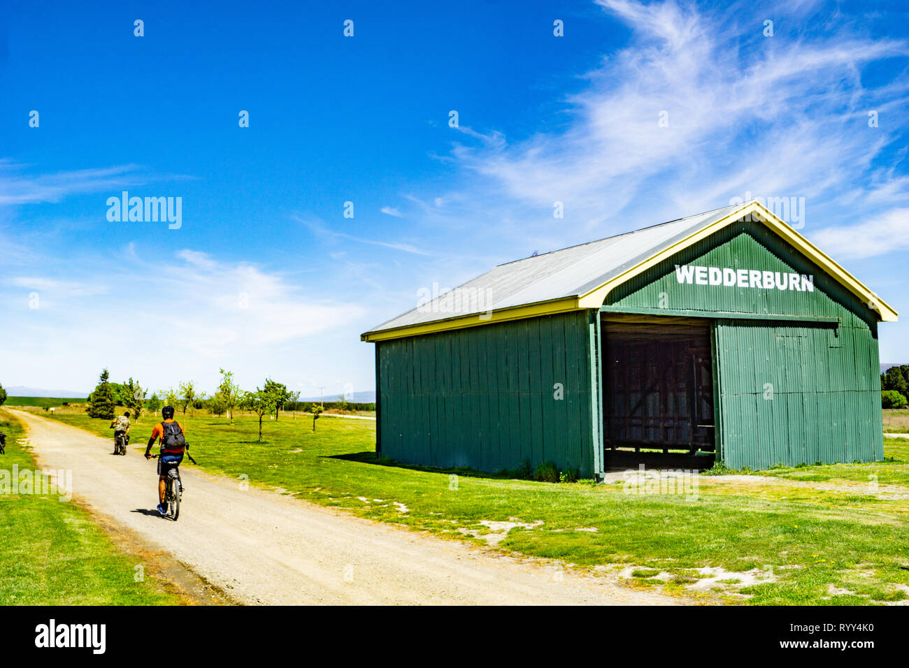 WEDDERBURN NUOVA ZELANDA - Ottobre 22 2018; su Central Otago Rail Trail ciclisti passando il vecchio punto di riferimento verde capannone ferroviario Foto Stock