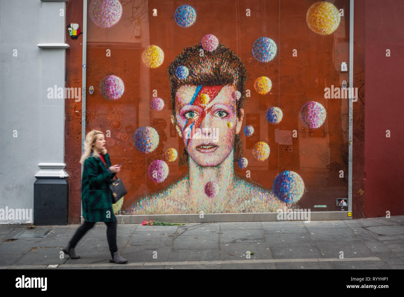 Londra, Inghilterra - Dicembre 2018 : la donna a piedi nella parte anteriore del graffiti in memoria del cantante David Bowie come Ziggy Stardust, Brixton Foto Stock