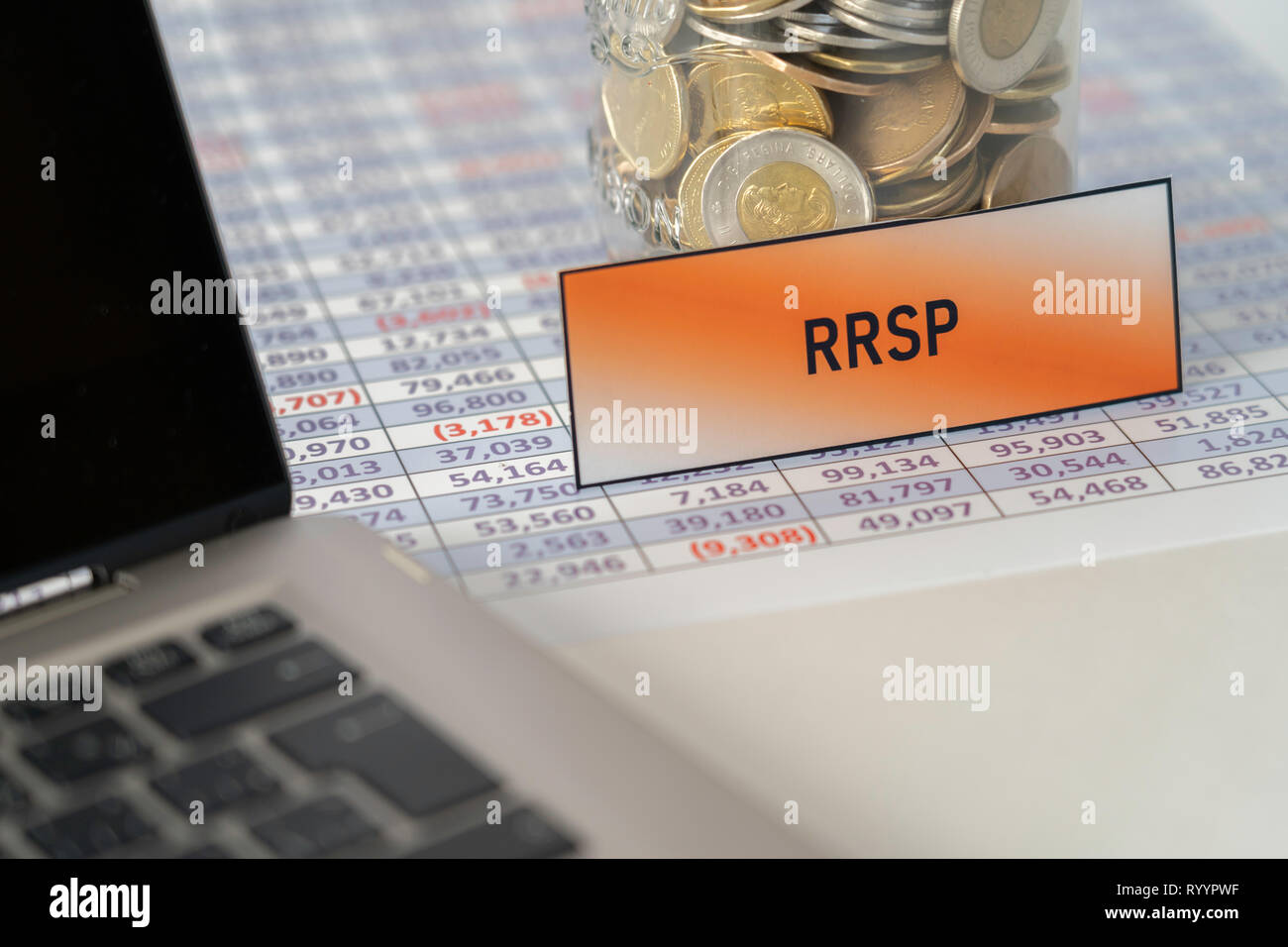 Vaso pieno di monete per RRSP sul foglio di calcolo accanto al laptop Foto Stock