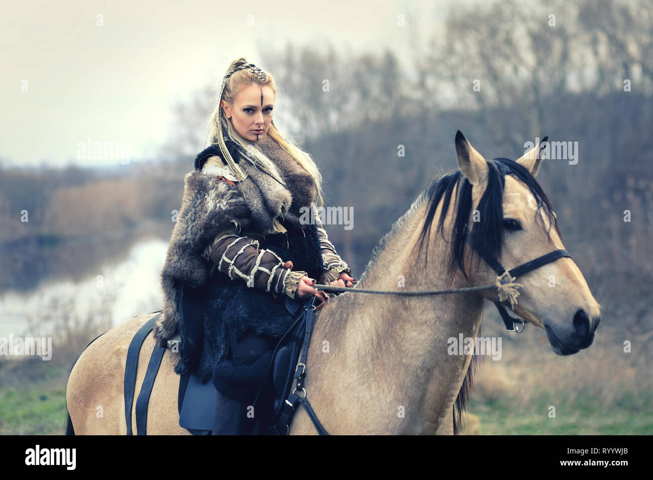 Viking warrior donna con capelli intrecciati e faccia dipinta di equitazione in foresta Foto Stock