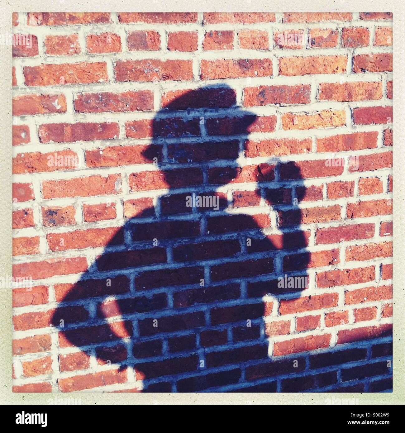 L ombra di un uomo contro un muro di mattoni Foto Stock