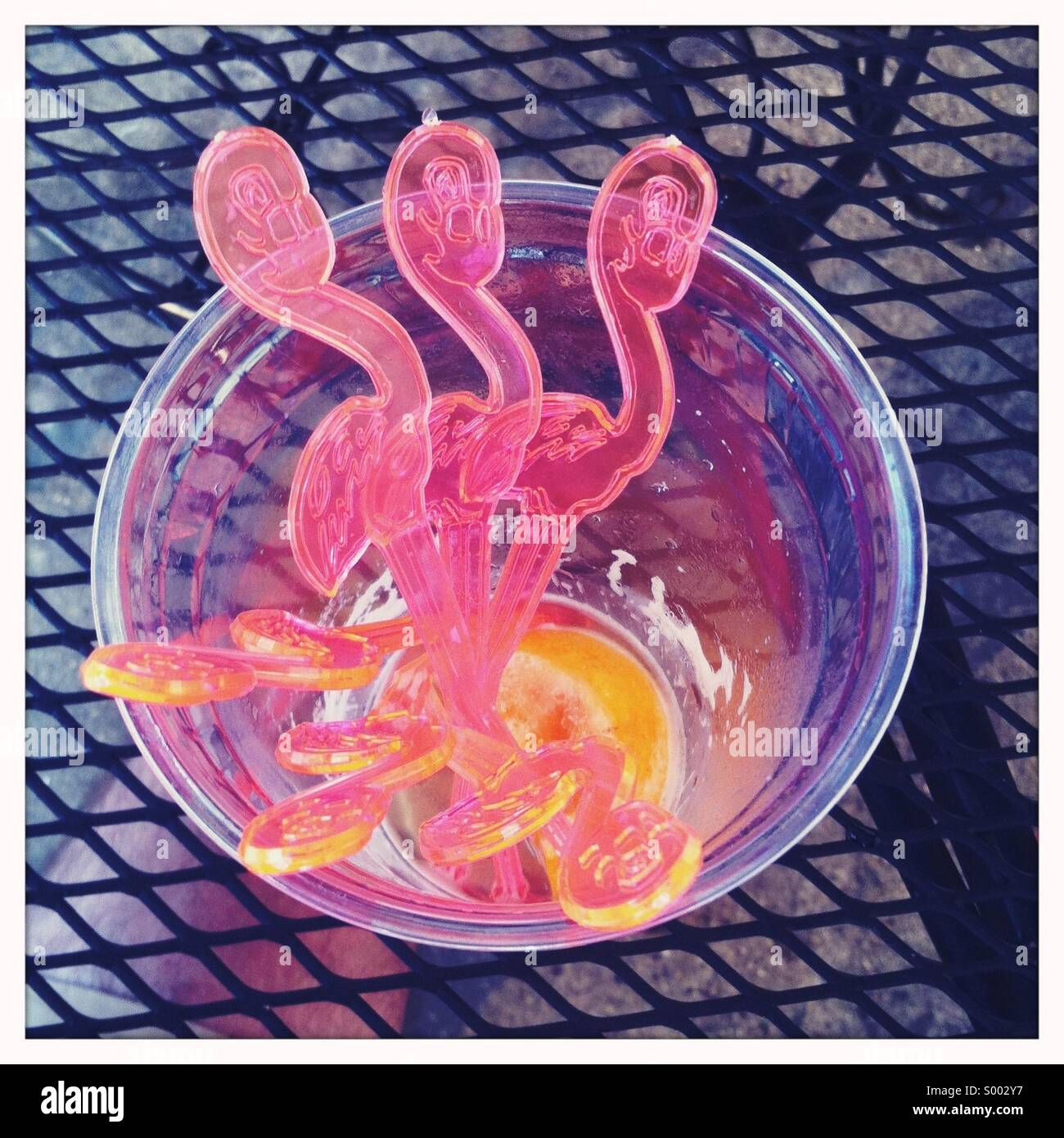 Un bicchiere di plastica con cocktail di benvenuto e sette fenicotteri in plastica agitare bastoni Foto Stock