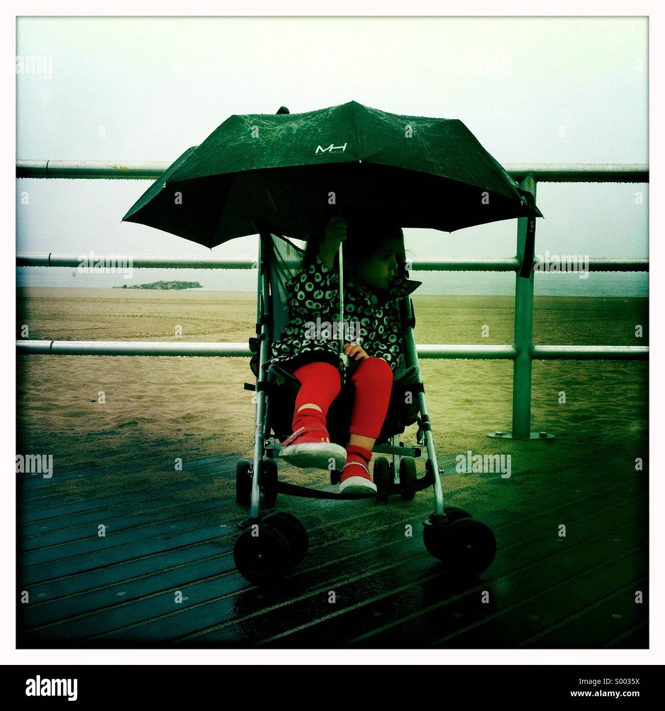 Una giovane ragazza in un passeggino che si nasconde sotto un ombrello Foto Stock