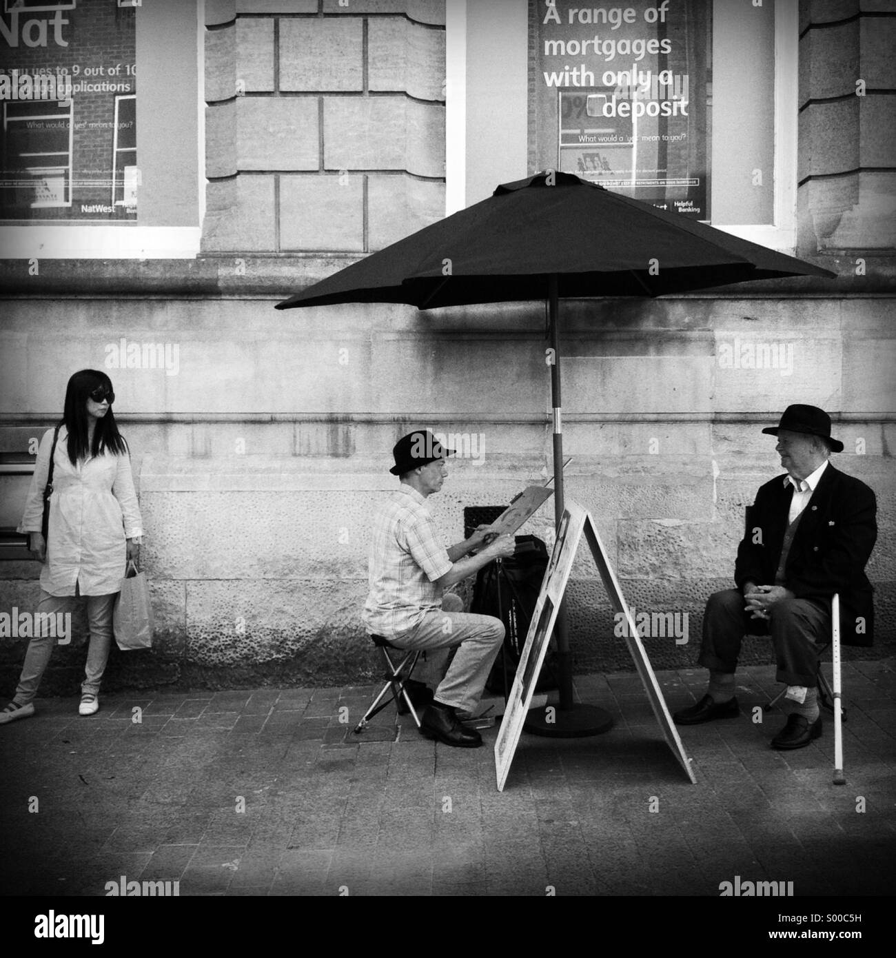 Un artista dipinge un uomo più anziano sotto un ombrellone mentre una signora guarda su Foto Stock