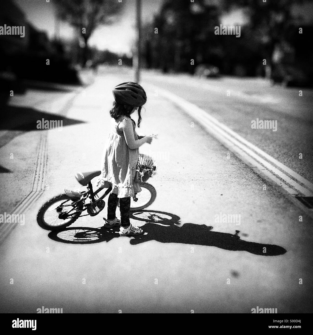 Ragazza giovane con la sua bicicletta e un cesto di fiori. Forte sole e ombra Foto Stock