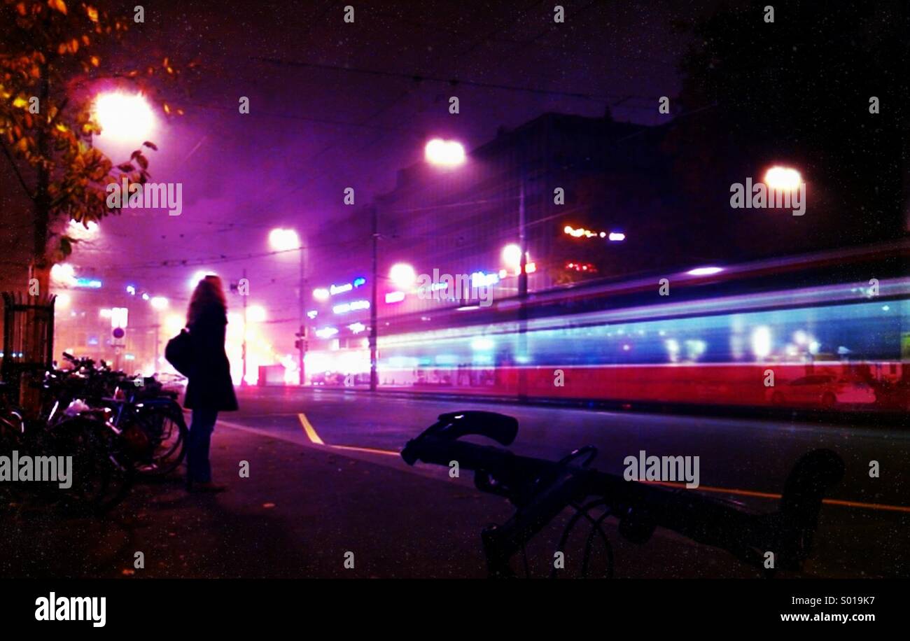 Una femmina di lone stagliano figura, guardando un tram rosso accelerando da - Attesa per l'ultimo bus home, Berna, Svizzera Foto Stock