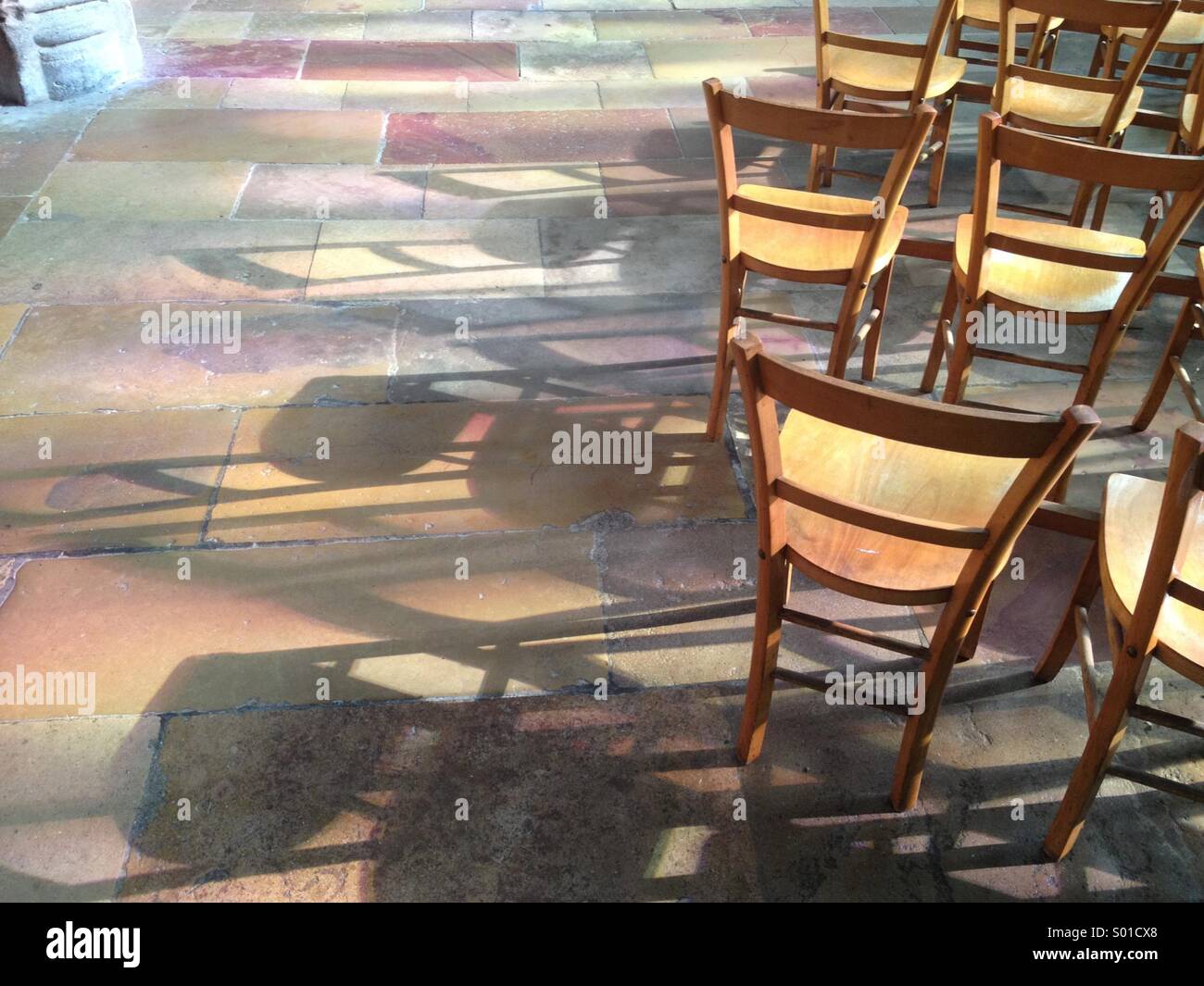 Giochi di luce attraverso la chiesa vetrate sul pavimento in pietra che gettano ombre di sedie Foto Stock