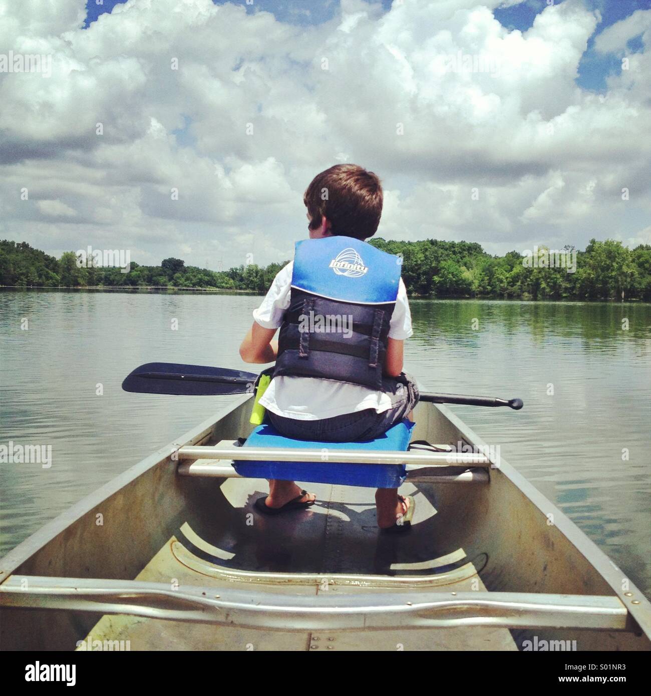Un ragazzo si siede in una canoa sulle sponde di un lago in un pomeriggio soleggiato Foto Stock