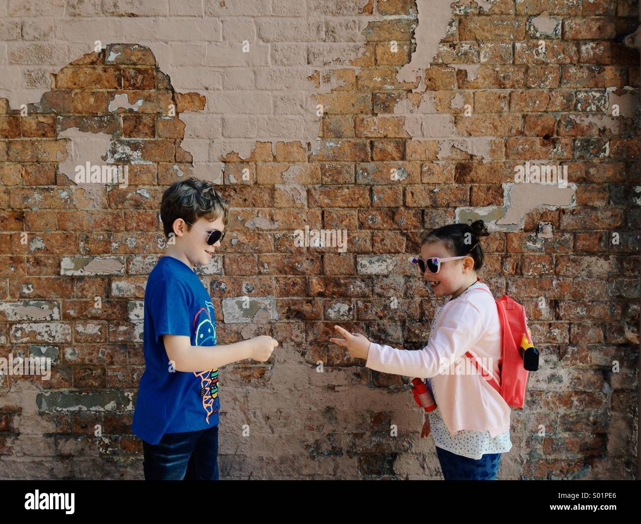Due bambini, un ragazzo e una ragazza che suona rock carta forbici nella parte anteriore di un muro di mattoni. Colore. Foto Stock