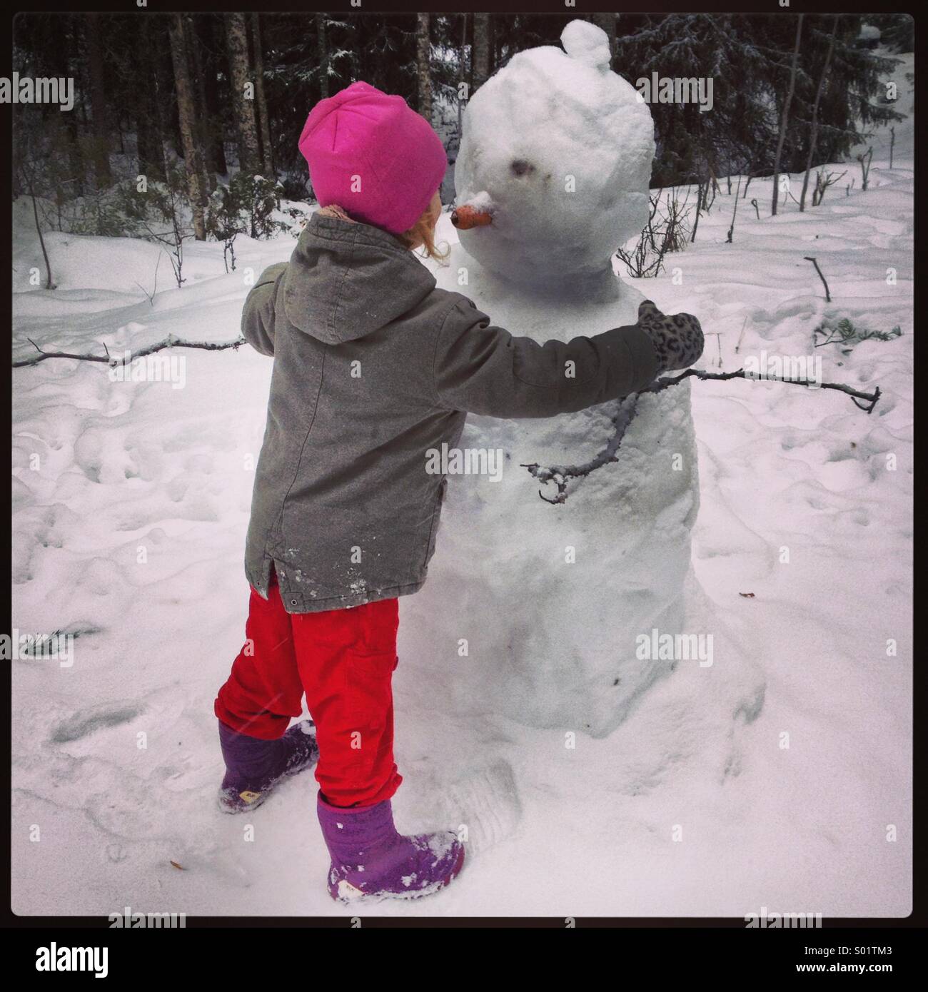 Una giovane ragazza che abbraccia un pupazzo di neve Foto Stock