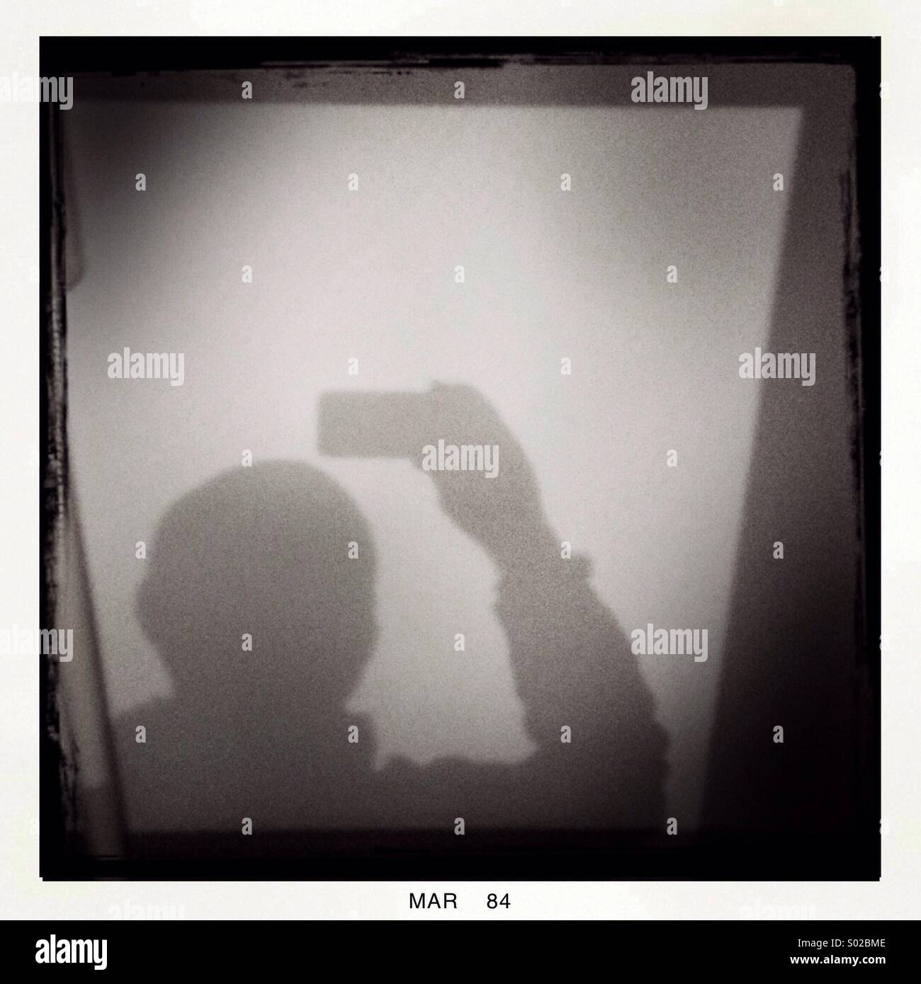 Un ombra di un uomo in possesso di un dispositivo mobile è visto. Foto Stock