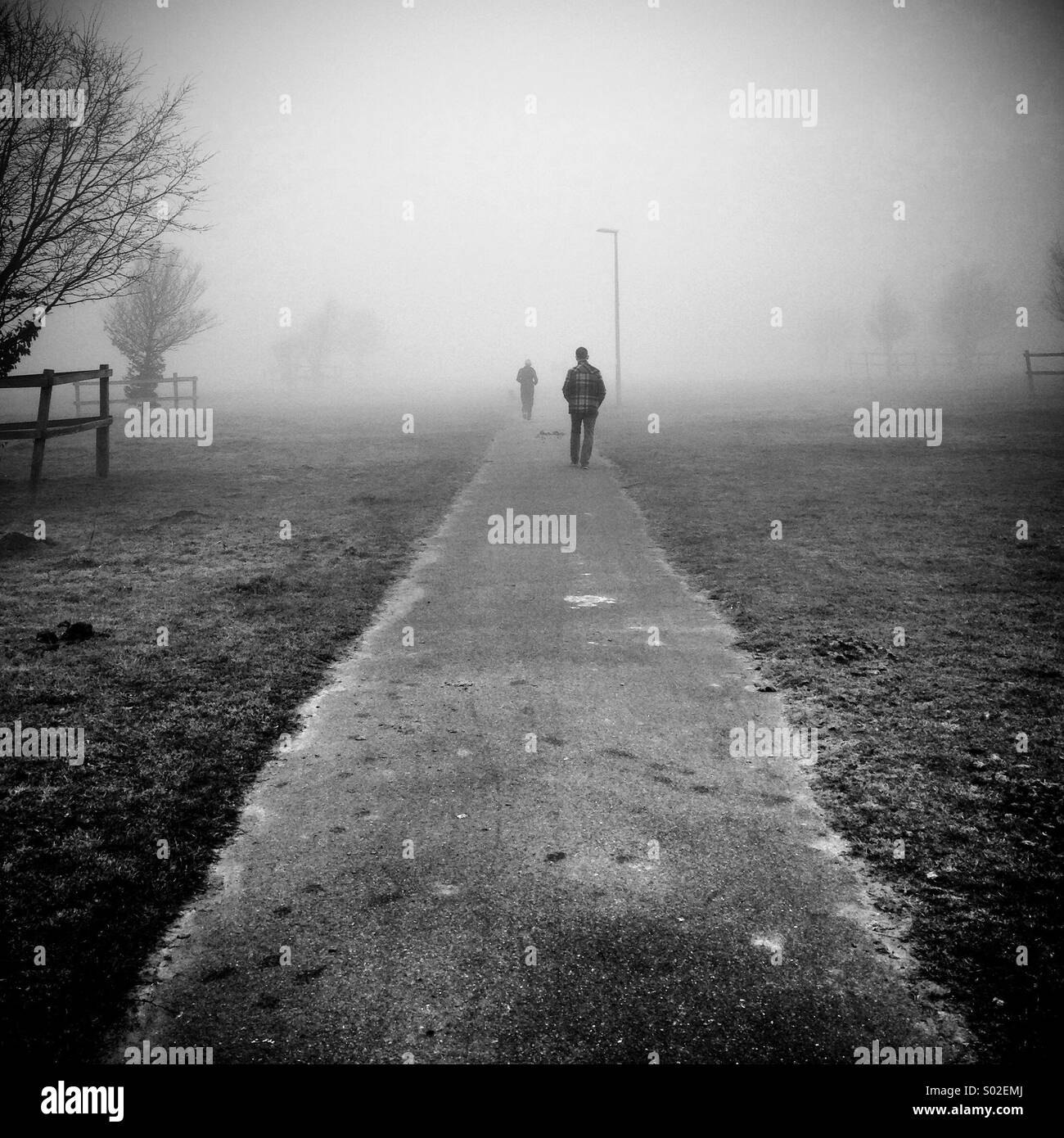 Due figure a piedi dalla fotocamera uno davanti all'altro lungo un percorso isolato attraverso la nebbia Foto Stock