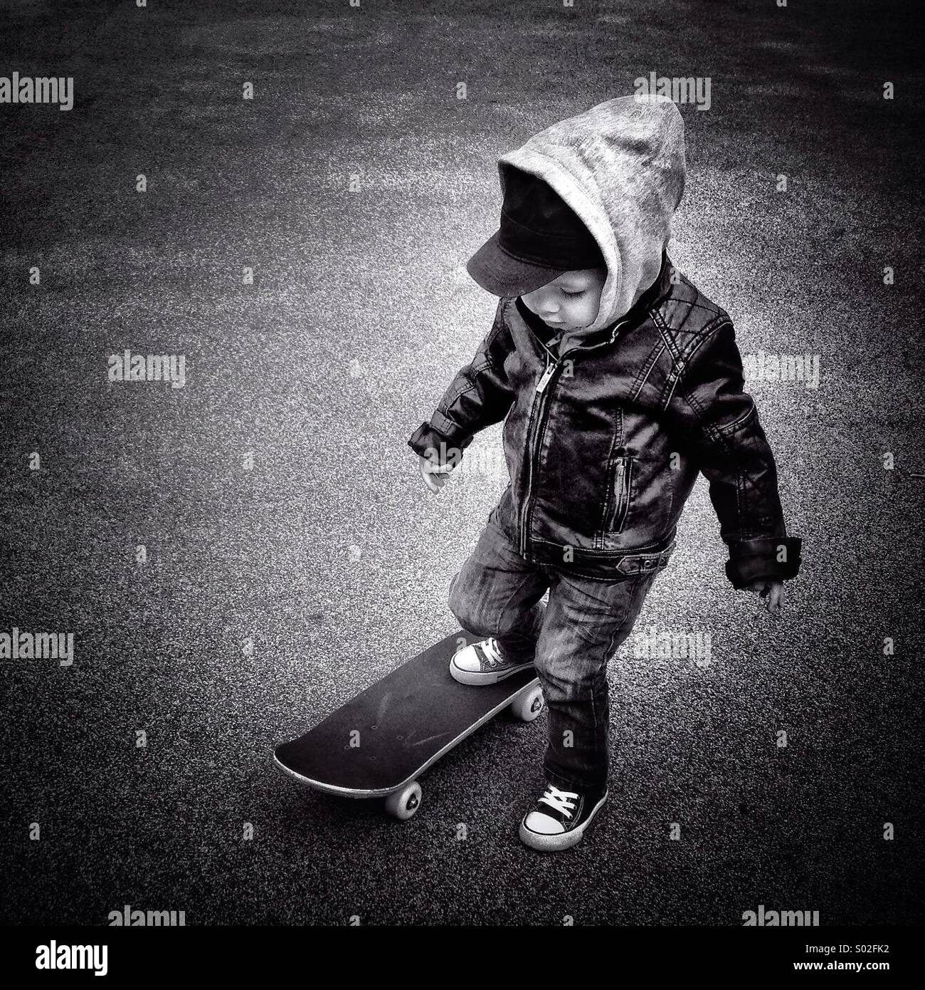 Bambino con la giacca di pelle che sta provando uno skateboard Foto Stock