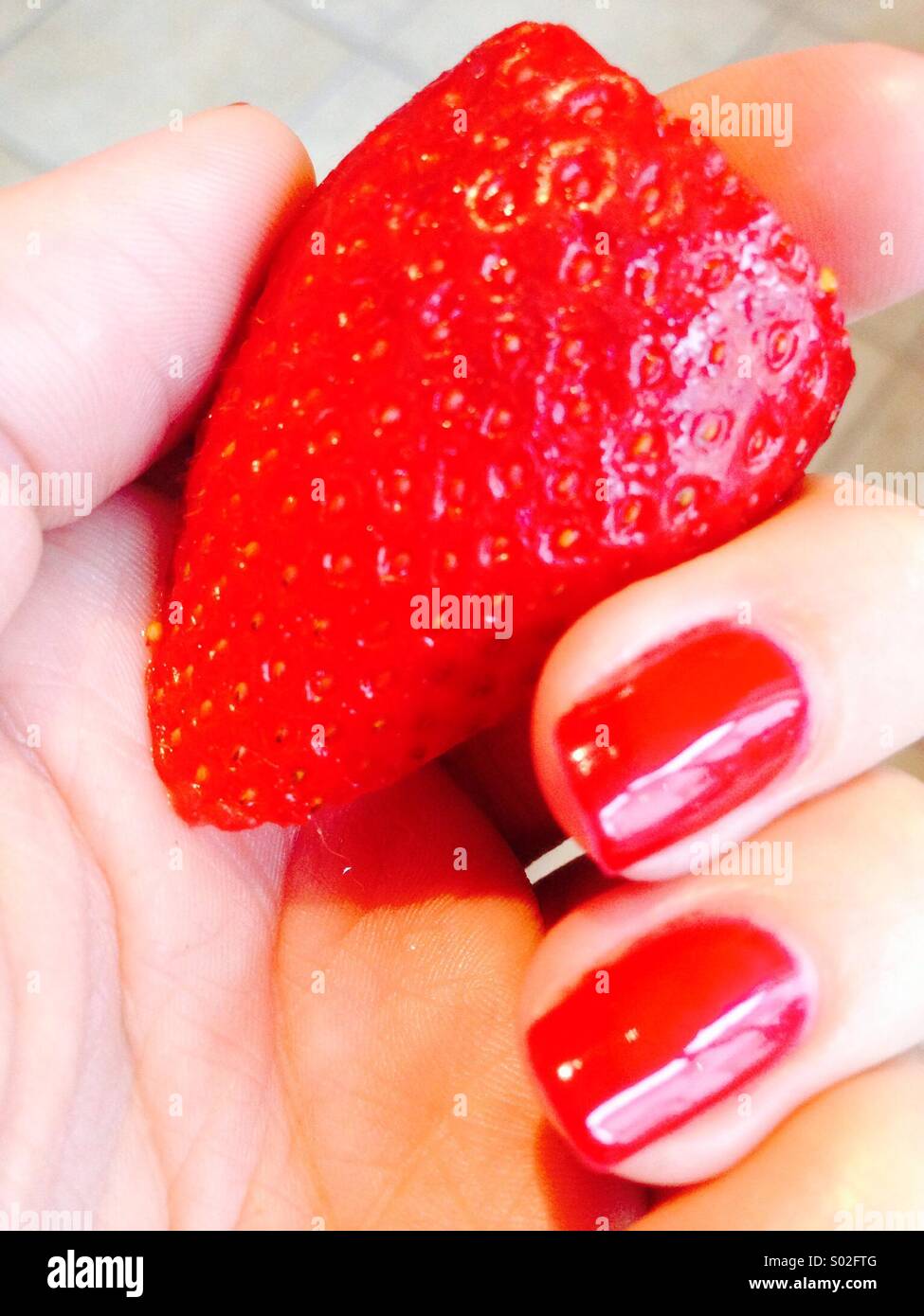 Fragola tenuto a mano con le unghie dipinte di rosso Foto Stock
