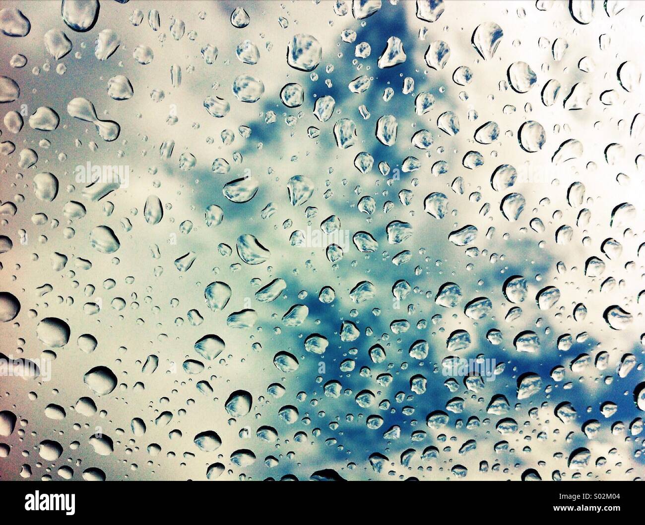Grandi gocce di acqua in auto parabrezza, al di fuori della messa a fuoco delle nuvole e del cielo in background. - Immagine stock catturata con smartphone