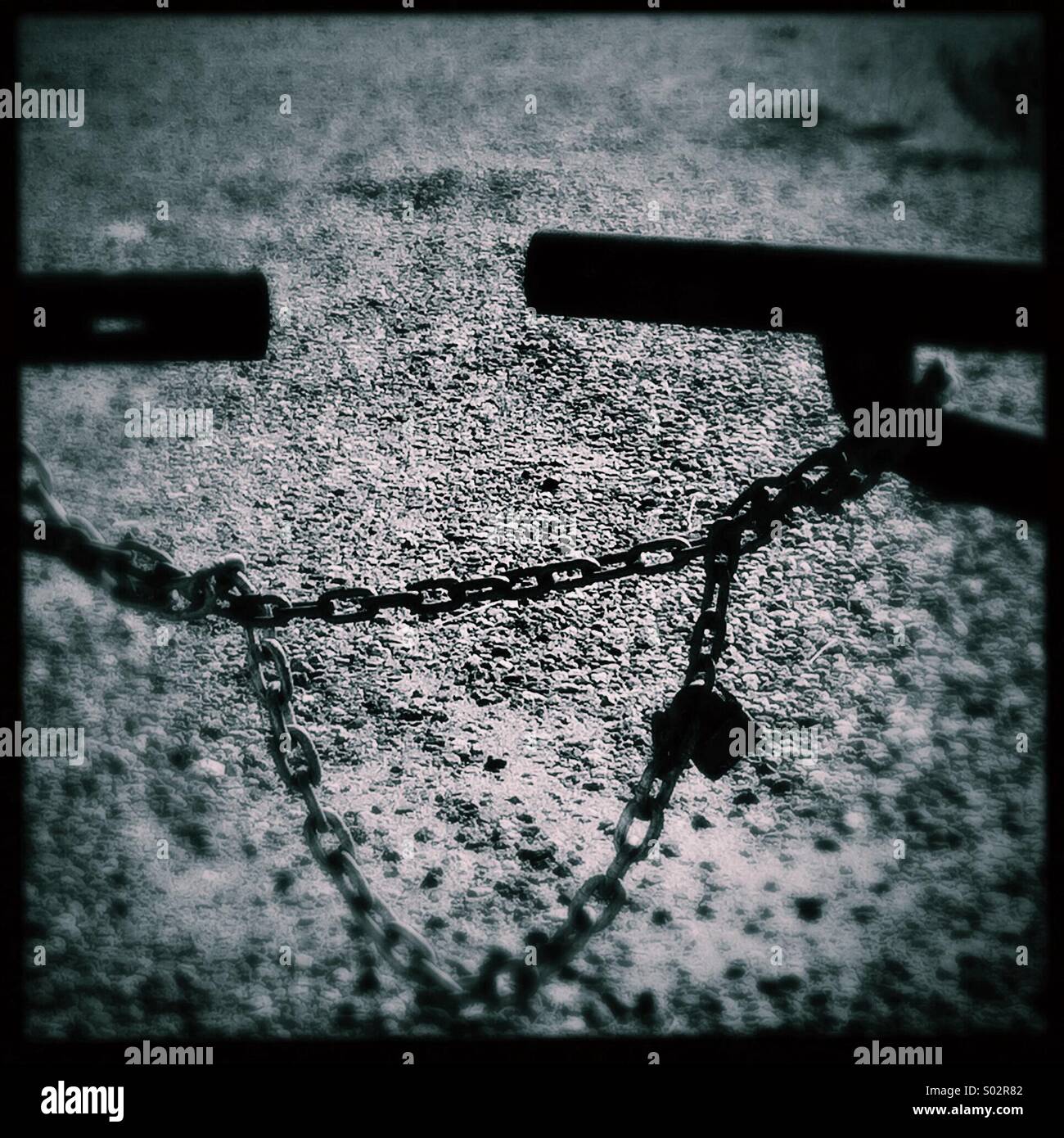 Barriera all'ingresso. Cancello chiuso in metallo con catena e lucchetto con ghiaia sullo sfondo. - Immagine stock catturata con smartphone