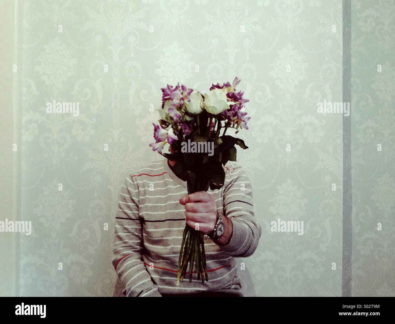 Figura nascosta presentando un mazzo di fiori in ambienti chiusi contro un semplice sfondo tappezzate Foto Stock