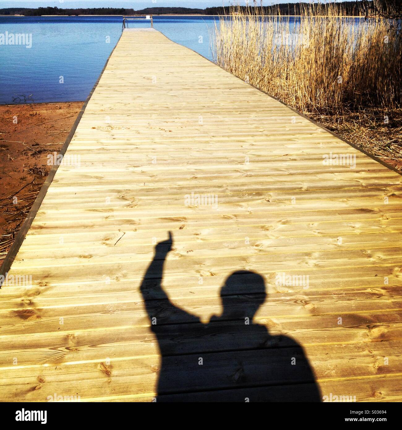 Un uomo in ombra rivolta lungo un lungo molo su di una spiaggia pubblica in Nordic Scandinavia Foto Stock